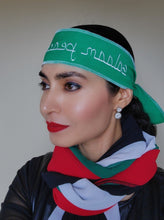 Woman wearing green headband with embroidered text in white reading "Peace, Salaam".